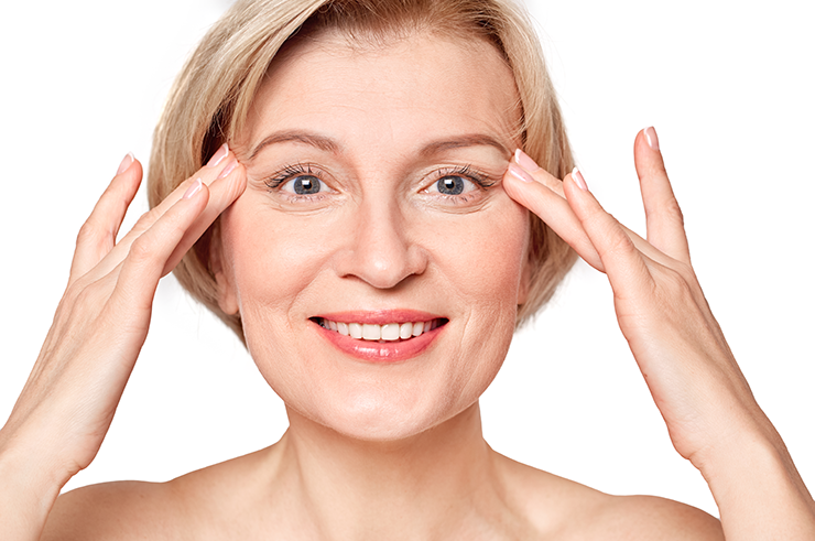 Middle-aged woman smiling, touching both sides of her face with fingertips, against a white background—showcasing the confidence that fillers and Botox can provide.